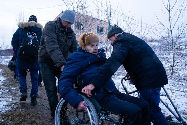 Чоловіки допомагають евакуюватись літній людині на візку. Ірпінь. Біля підірваного мосту.