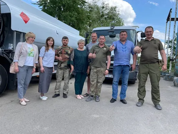 Олександр Ковальчук (у синій сорочці) фотографується на фоні двох машин для воїнів
